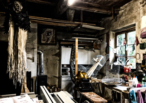 Einblick in die Werkstatt. Auf dem Werkstatttisch stehen gedrahtete Zylinder und ein Sauenkopf, sowie ein historischer Taucherhelm und eine Plastik Krakenarm.